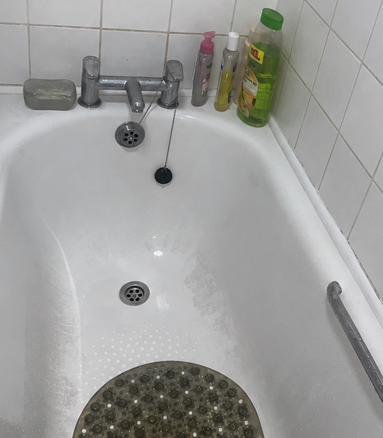 Bath before cleaning, with soap scum and a dirty mat